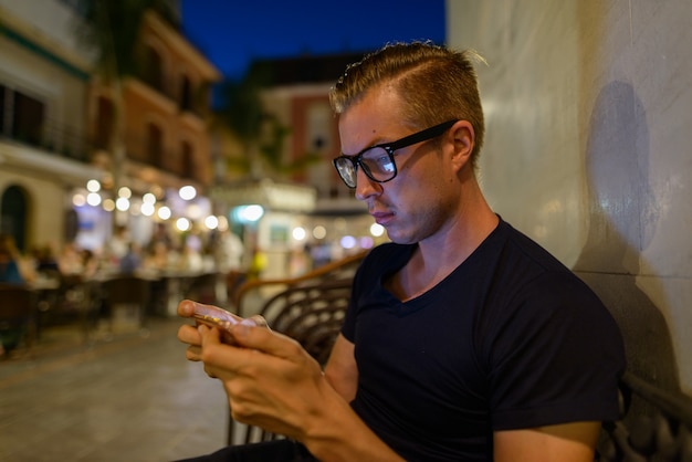 Porträt des jungen gutaussehenden Touristenmannes, der am Restaurant draußen sitzt