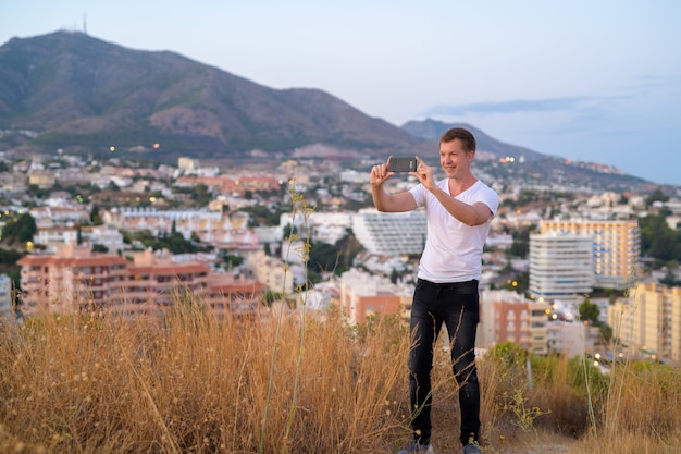 Porträt des jungen gutaussehenden Touristenmannes oben auf dem Hügel, der die Stadt Malaga, Spanien überragt