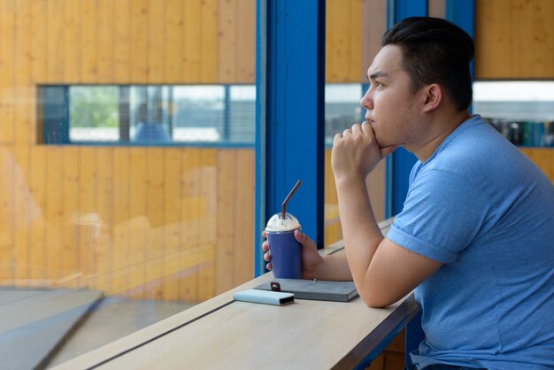 Porträt des jungen gutaussehenden übergewichtigen philippinischen Mannes, der am Kaffeehaus entspannt