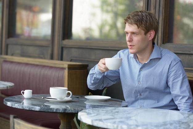 Porträt des jungen hübschen blonden Geschäftsmannes, der am Kaffeehaus draußen entspannt