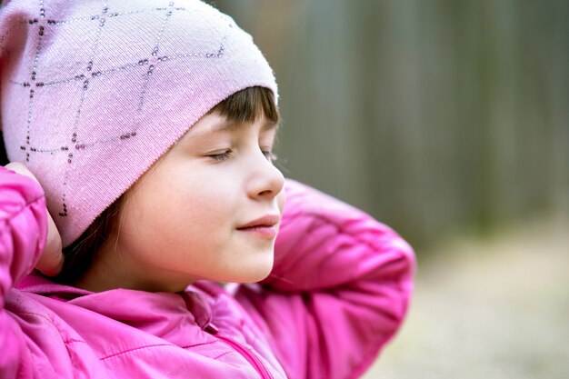 Foto porträt des jungen hübschen kindermädchens, das rosa jacke und mütze trägt, die warmen warmen tag im frühen frühling draußen genießen.