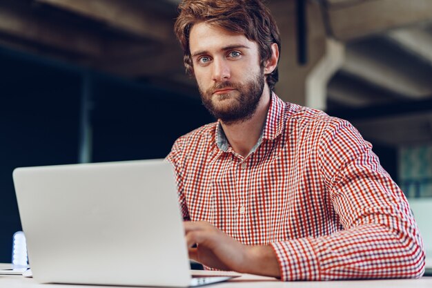 Porträt des jungen kaukasischen Geschäftsmannes, der Laptop-Computer an seinem Arbeitsplatz im modernen Büro verwendet