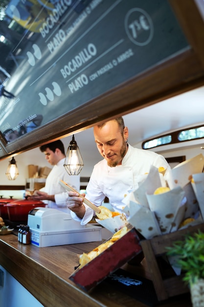 Foto porträt des jungen kochs, der grillkartoffeln in einem imbisswagen serviert.