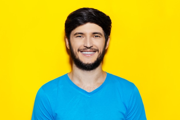 Porträt des jungen lächelnden Kerls, der blaues Hemd auf gelber Farbe trägt