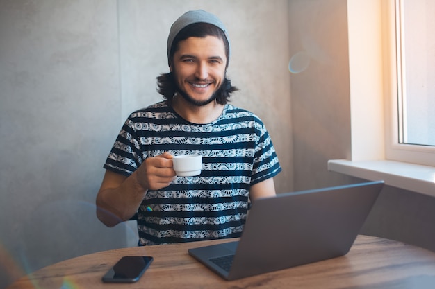 Porträt des jungen lächelnden Mannes, der Kaffee trinkt und nach Hause arbeitet.