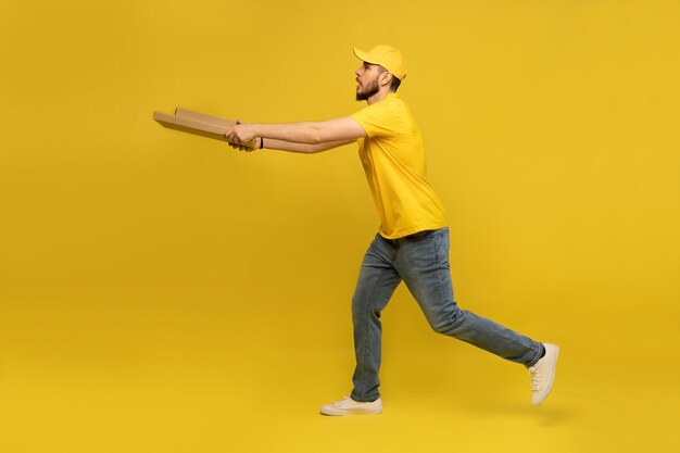 Porträt des jungen Liefermanns in der gelben Uniform mit Pizzaschachteln lokalisiert über gelber Wand