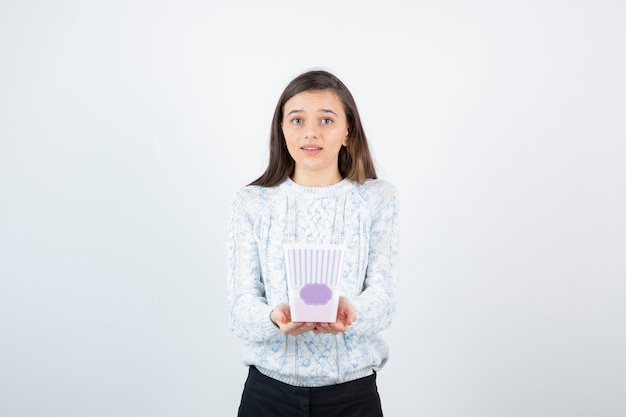 Porträt des jungen Mädchens im gestrickten Pullover, das leere Popcornschachtel zeigt.