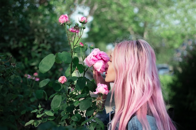 Porträt des jungen Mädchens mit rosa Haar, das Rosenblume schnüffelt.