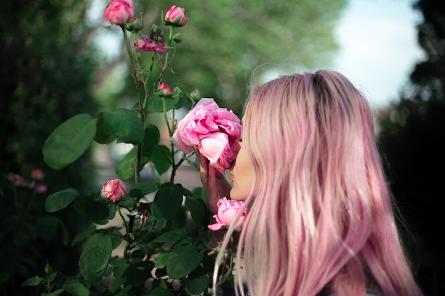 Porträt des jungen Mädchens mit rosa Haar, das Rosenblume schnüffelt.