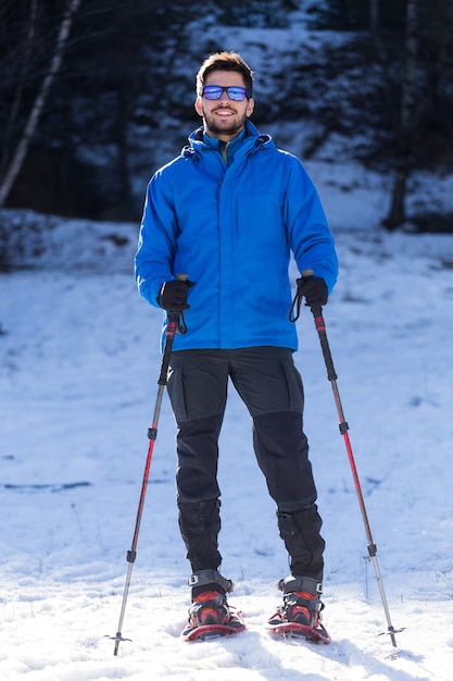 Porträt des jungen Mannes, der in Schneeschuhen über Winterhintergrund geht.