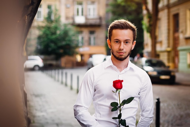 Porträt des jungen Mannes, der weißes Hemd trägt und eine Rose hält Ma