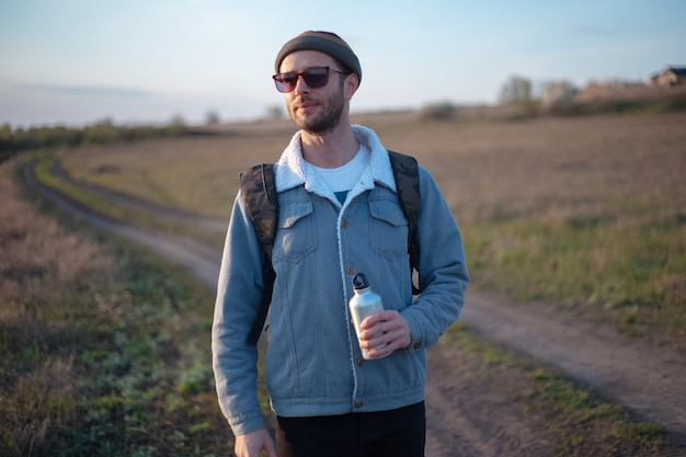 Porträt des jungen Mannes mit Rucksack, der wiederverwendbare Aluminium-Thermowasserflasche in der Hand hält