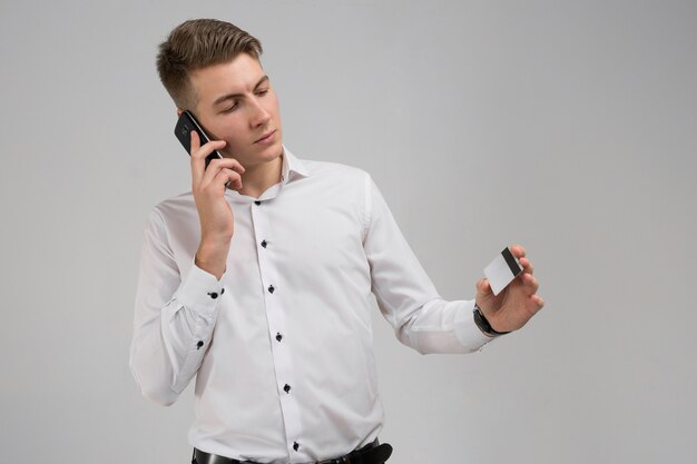 Porträt des jungen Mannes sprechend am Handy mit der Kreditkarte in der Hand lokalisiert auf Weiß