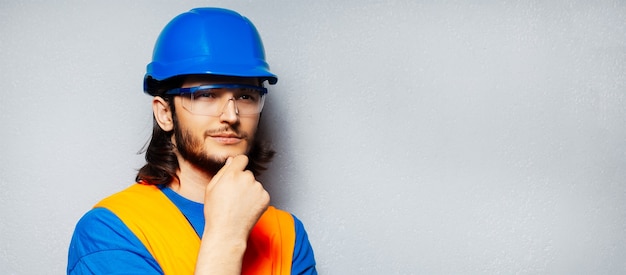 Porträt des jungen nachdenklichen Bauarbeiteringenieurs, der Sicherheitsausrüstung trägt