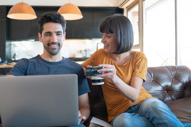 Porträt des jungen Paares, das online mit einer Kreditkarte und einem Laptop von zu Hause aus einkauft.