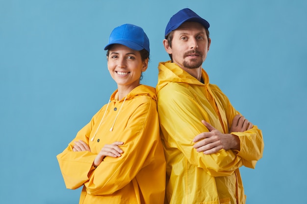 Porträt des jungen Paares in der Uniform, die im Lieferservice arbeitet, der mit verschränkten Armen steht und auf Blau lächelt