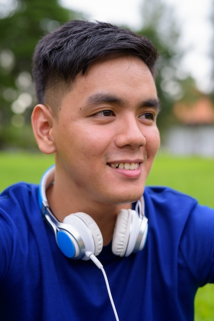 Porträt des jungen schönen asiatischen Mannes, der am Park in Bangkok, Thailand entspannt