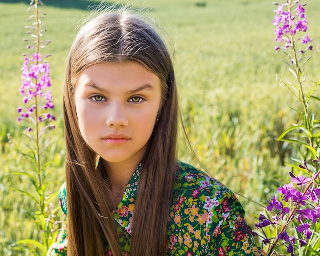 Porträt des jungen schönen Mädchenmodells, das in die Kamera auf grün blühendem Rasen unter lila Blumen schaut