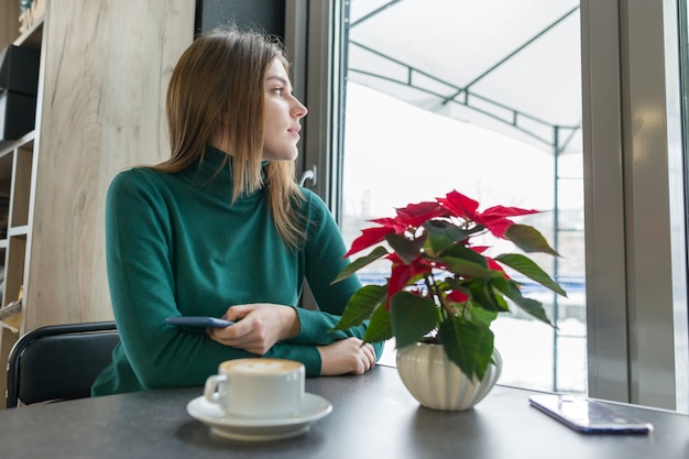 Porträt des jungen schönen Mädchens, das am Café sitzt