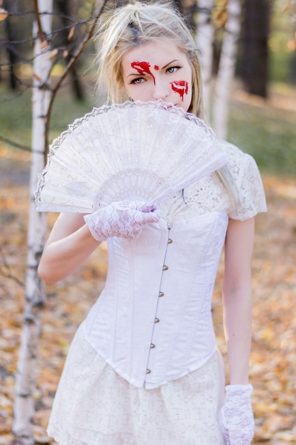 Porträt des jungen schönen Mädchens mit Bluthalloween-Make-up auf ihrem Gesicht und weißen Kleid