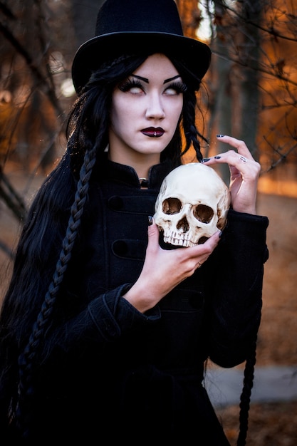 Porträt des jungen schönen Mädchens mit dunklem Make-up auf ihrem Gesicht und Skelett in den Händen