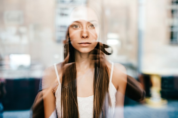 Porträt des jungen schönen romantischen brünetten Mädchens mit dem langen Haar, das hinter Glas aufwirft