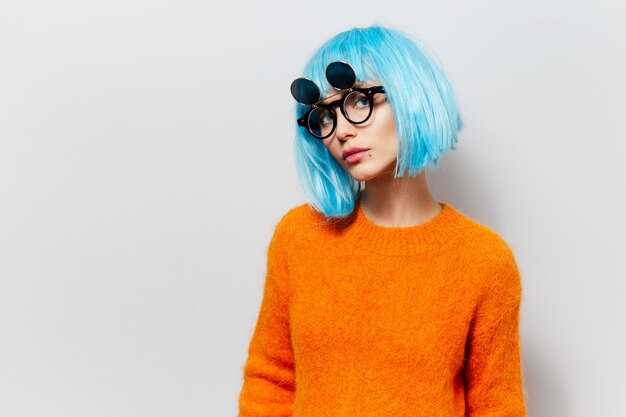 Porträt des jungen Schönheitsmädchens mit dem blauen Haar in der tragenden Sonnenbrille der orange Strickjacke auf weißem Hintergrund.