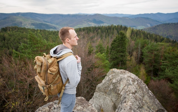 Porträt des jungen Touristen mit Rucksack steht auf den Felsen