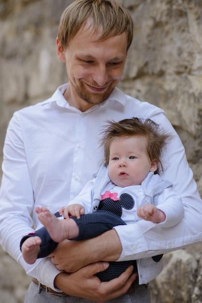 Porträt des jungen Vaters, der weinendes Baby über weißer Backsteinmauer hält