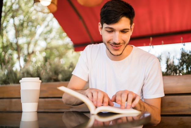 Porträt des kaukasischen Mannes, der Freizeit genießt und ein Buch liest, während draußen im Coffeeshop sitzt. Lifestyle-Konzept.