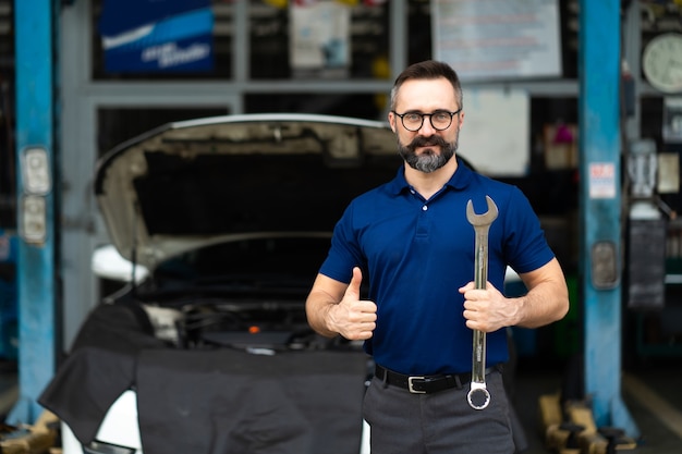 Porträt des kaukasischen Mannes, der zur Kamera und zu großen Schlüsselwerkzeugen in der Hand lächelt. Fachmechaniker in der Autowerkstatt.