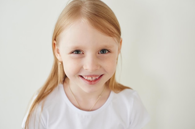 Porträt des kleinen blonden Mädchens auf weißem Hintergrund im weißen T-Shirt