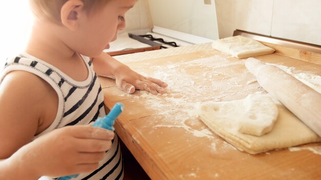 Porträt des kleinen Jungen, der Teig auf hölzerner Küchenarbeitsplatte macht