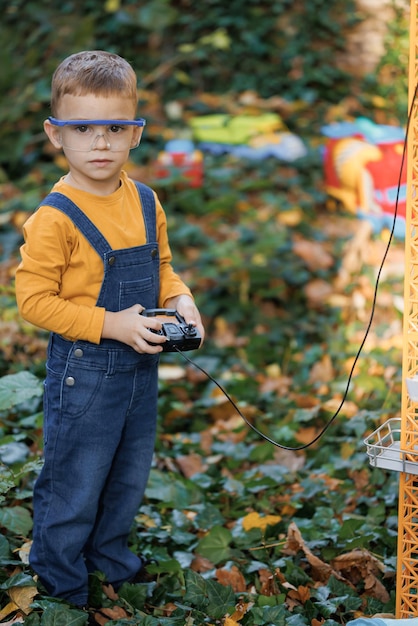 Porträt des kleinen Jungen mit ferngesteuertem Kranbalken in einem Industrielager Ingenieur des kleinen Jungen