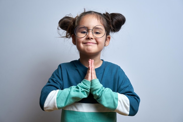 Porträt des kleinen kaukasischen Mädchens faltete ihre Hände in Gebetsgeste isoliert auf weißem Hintergrund Friedliches, dankbares, vertrauensvolles Konzept