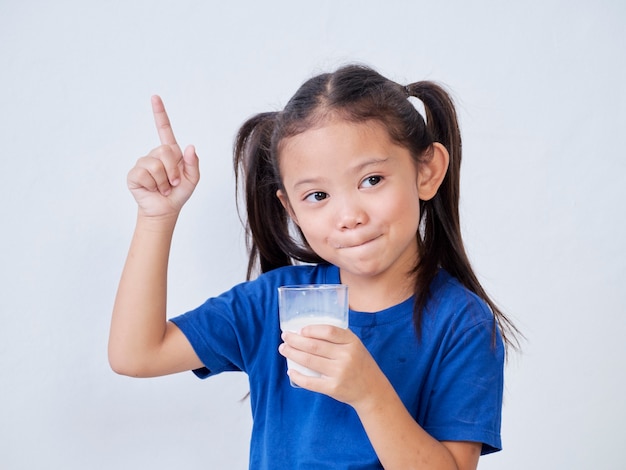 Porträt des kleinen Mädchens, das Milch trinkt und auf hellgrau zeigt