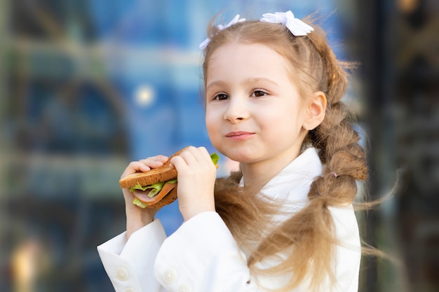 Foto porträt des kleinen mädchens, das während der pause zwischen den klassen sandwich isst. gesundes ungesundes essen für kinder. frühstück mittagessen für kinder in der schule.