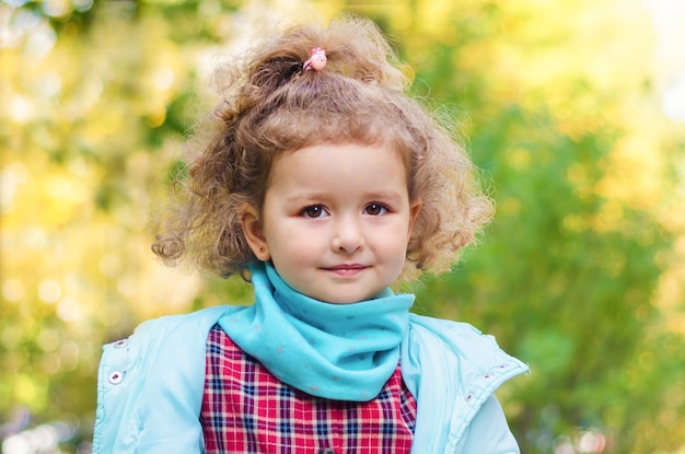 Porträt des kleinen niedlichen lächelnden Mädchens mit Locken am Herbsttag.