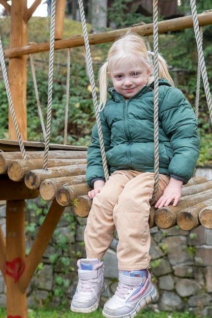 Porträt des kleinen Verlegenheitsmädchens im Herbst auf Hängebrücke oder Spielplatz Mädchen mit zwei Pferdeschwänzen auf dem Spielplatz