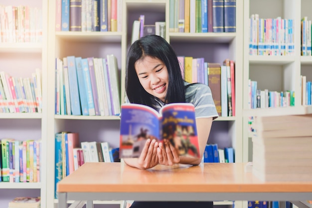 Porträt des klugen asiatischen Studenten, der Forschung in der Collegebibliothek liest und tut