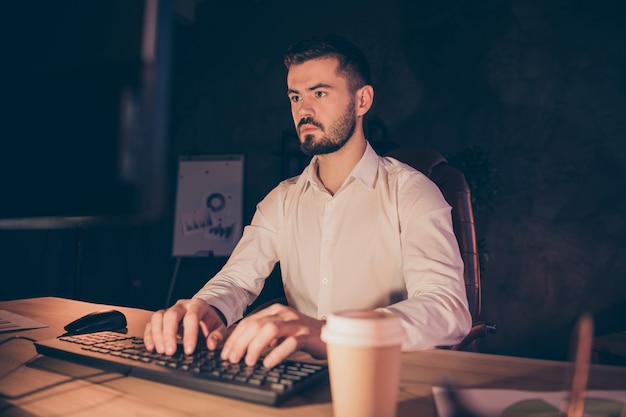 Porträt des konzentrierten Geschäftsmannes bleiben in der Nacht im dunklen Büro, das am Computer arbeitet