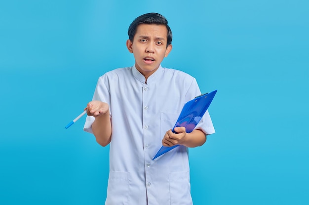 Porträt des Krankenpflegers, der Klemmbrett und Stift mit überraschtem Gesicht auf blauem Hintergrund hält