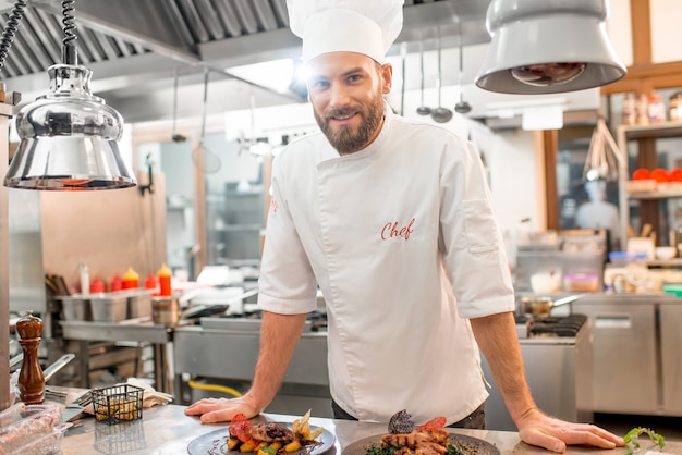 Porträt des Küchenchefs in Uniform mit zubereitetem köstlichem Gericht in der Restaurantküche