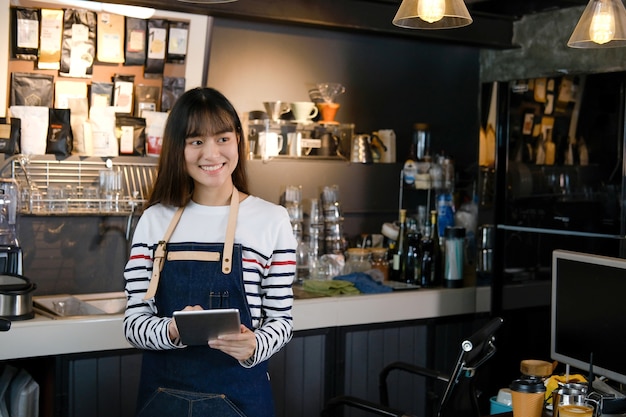 Porträt des lächelnden asiatischen barista, das digitale Tablette am Zähler in der Kaffeestube hält