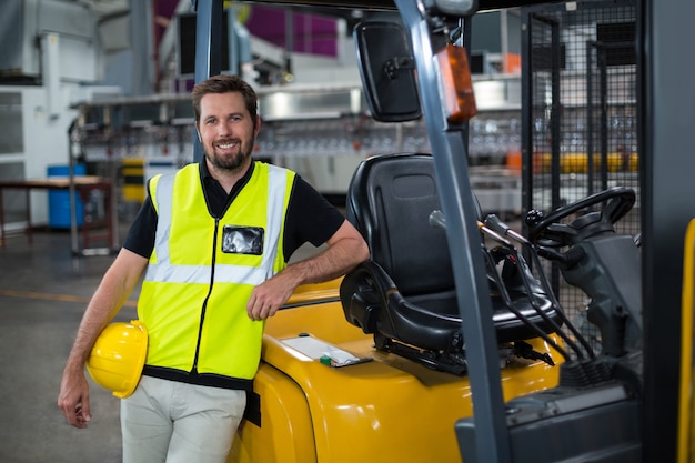 Porträt des lächelnden Fabrikarbeiters, der sich auf Gabelstapler stützt