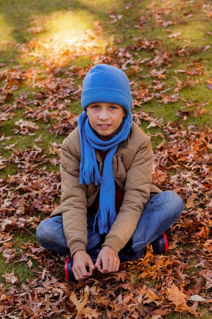 Porträt des lächelnden Jungen, der im Park im Herbst sitzt