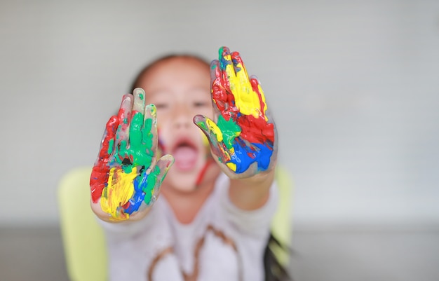 Porträt des lächelnden kleinen Mädchens, das durch ihre bunten Hände und Backe gemalt im Kinderraum schaut.