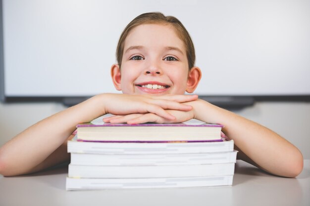 Porträt des lächelnden Mädchens, das sich auf Stapel Bücher im Klassenzimmer stützt