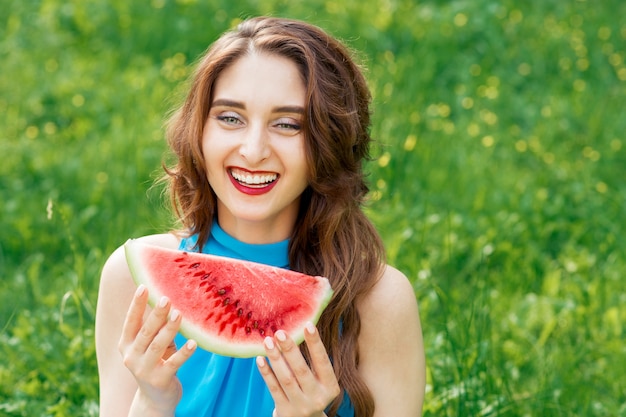 Porträt des lächelnden Mädchens mit Scheibe der Wassermelone auf Hintergrund des grünen Grases.