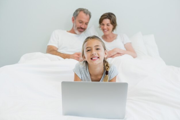 Porträt des lächelnden Mädchens unter Verwendung des Laptops, während Eltern im Hintergrund ruhen